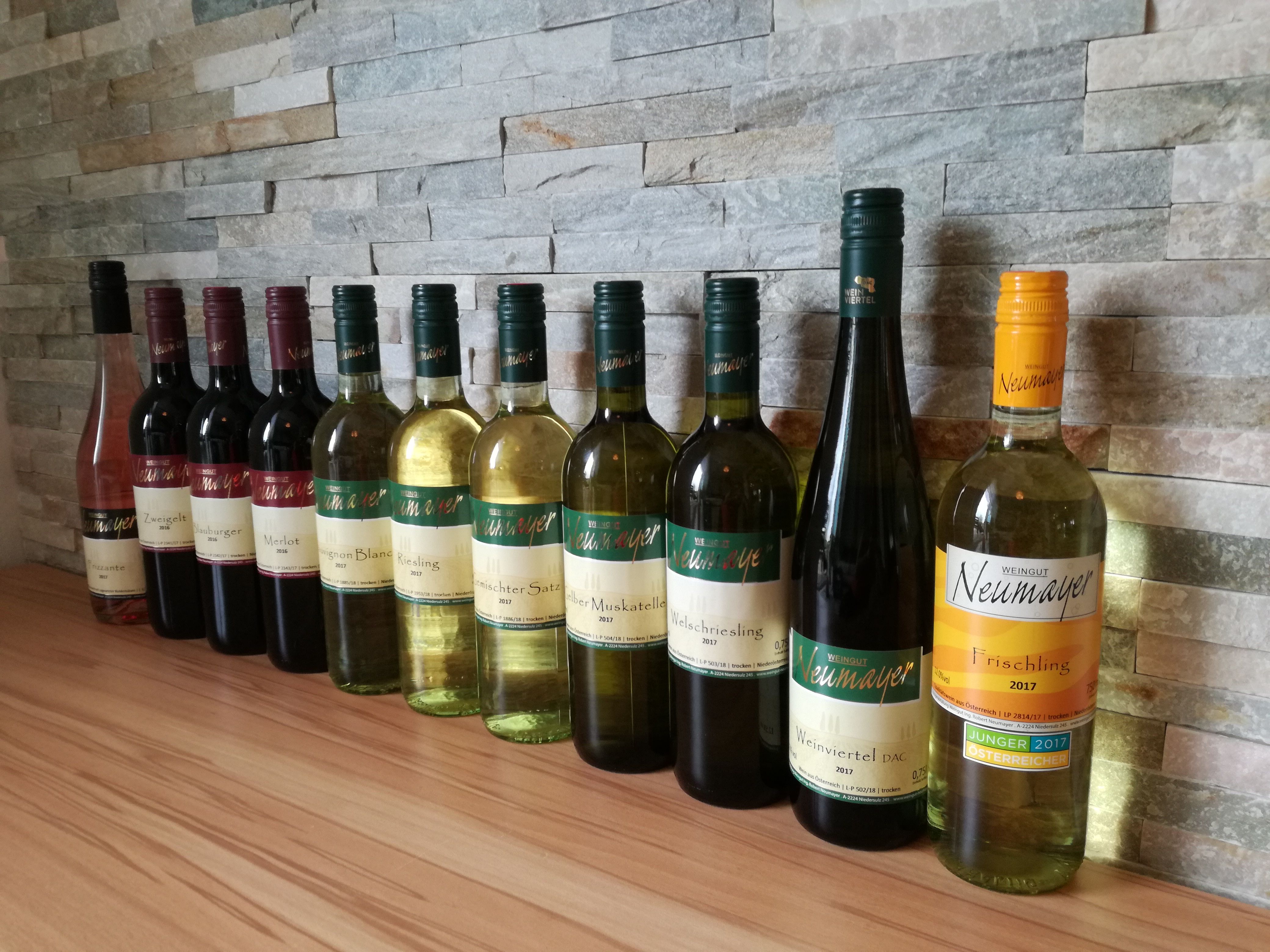 Eine Reihe von Weinflaschen des Weinguts Neumayer vor einer Steinwand.