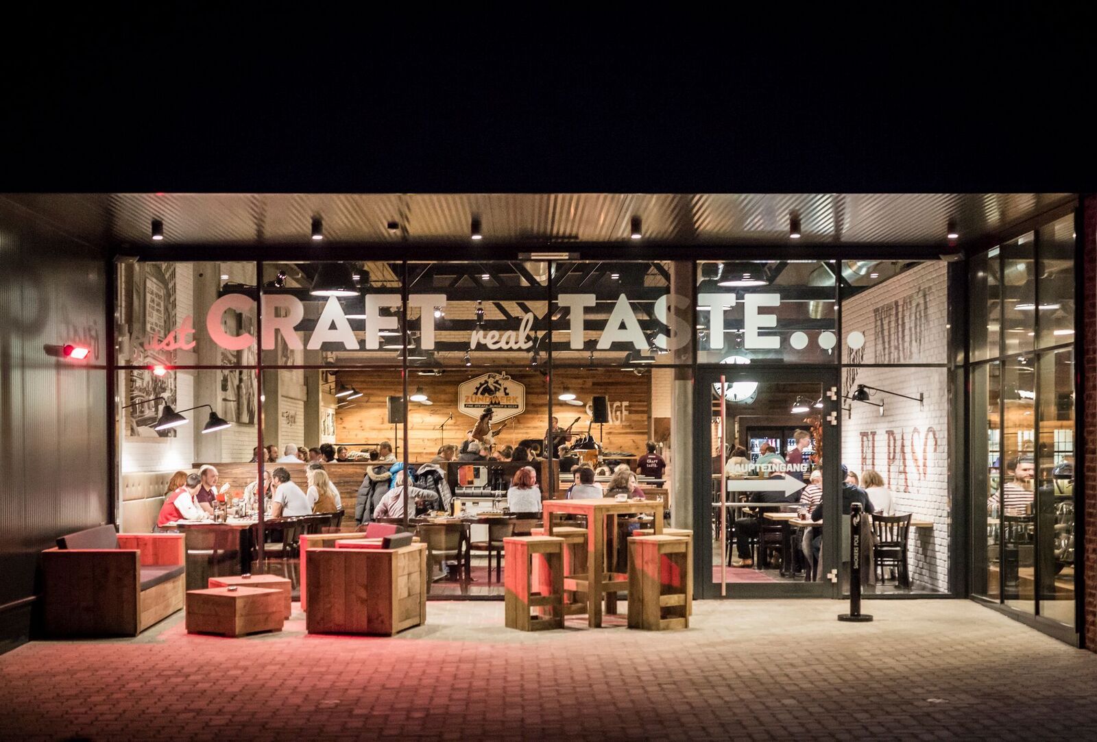 Außenansicht eines Restaurants mit Glasfront, innen sitzen Menschen an Tischen.