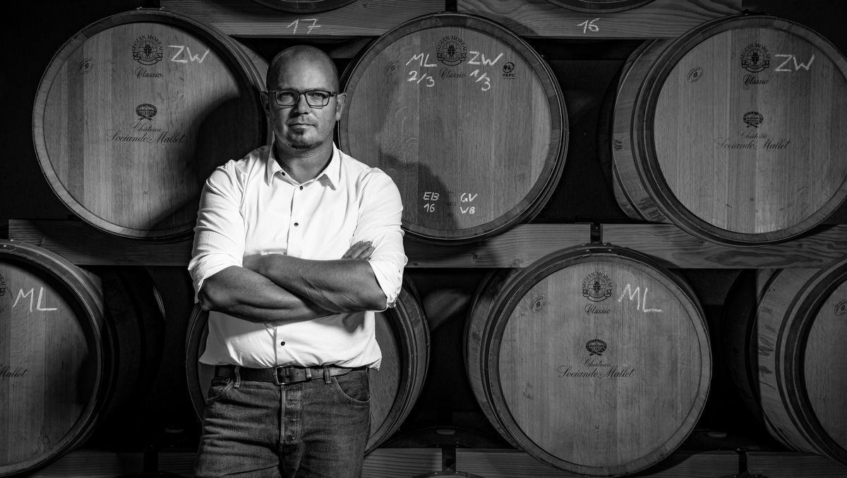 A man stands with his arms folded in front of several wine barrels.