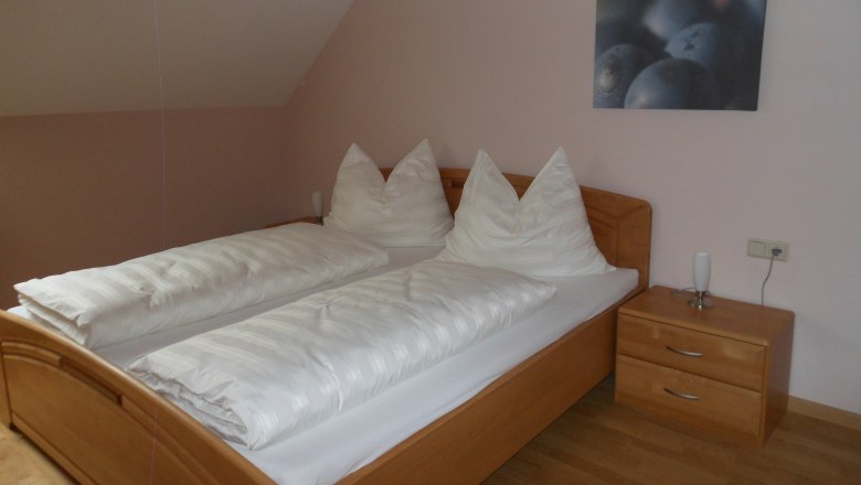 Ein schlichtes Gästezimmer mit einem Doppelbett, weißen Bettdecken und einem Nachttisch mit Lampe.