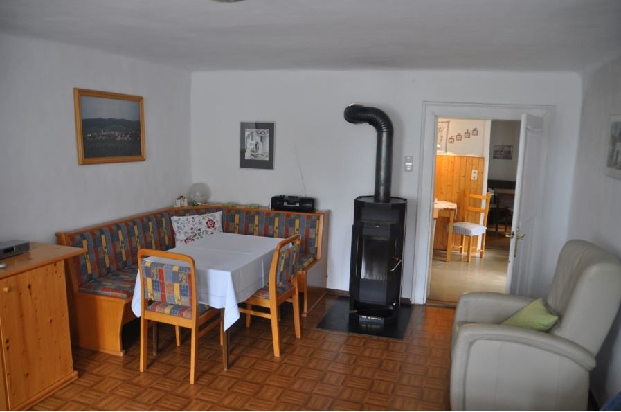 Gemütliche Essecke mit Eckbank, Tisch und Stühlen, daneben ein Ofen. Im Hintergrund ein Durchgang zu einem weiteren Raum.