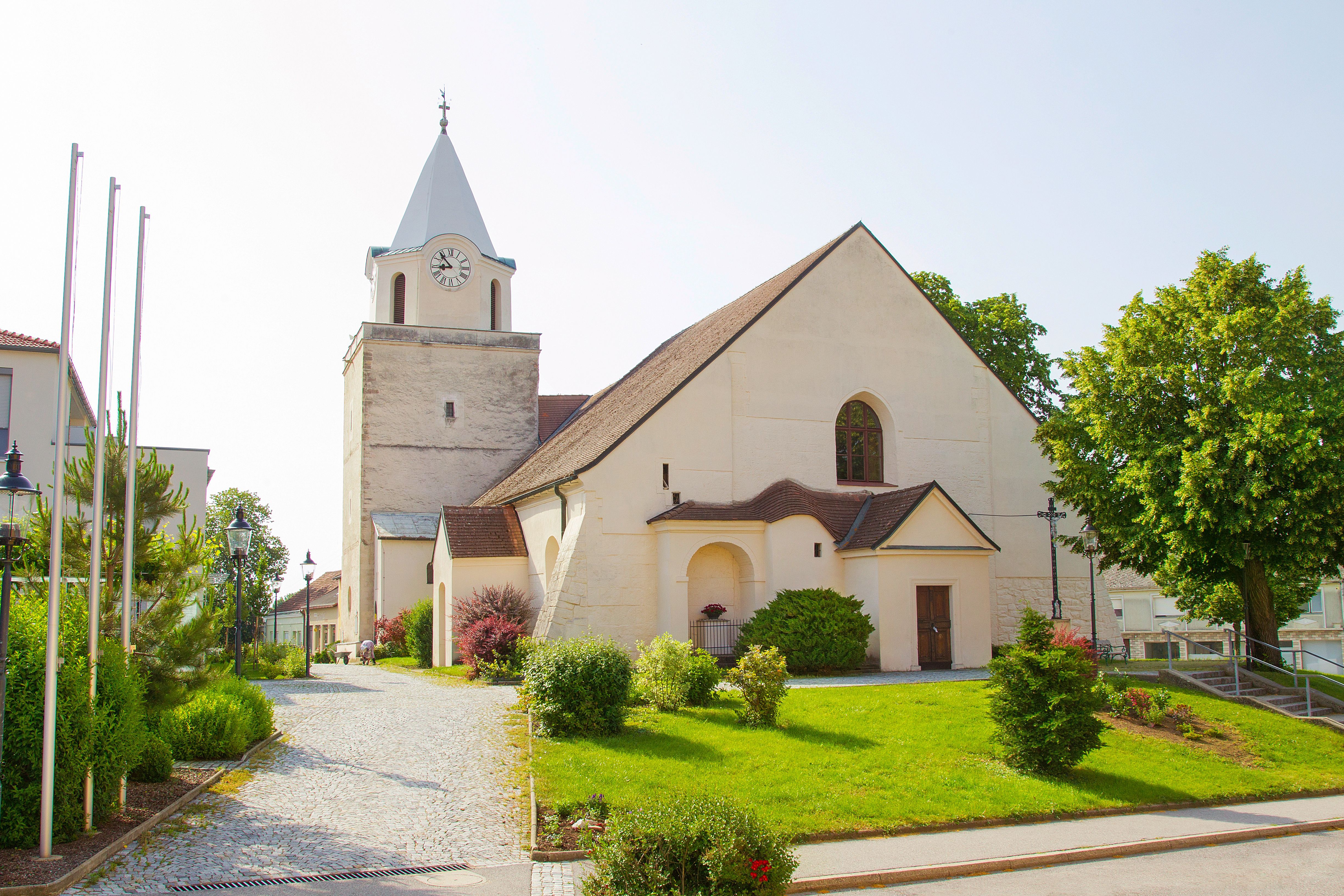 Kostel s věží a hodinami, obklopený udržovanou zahradou a stromy.