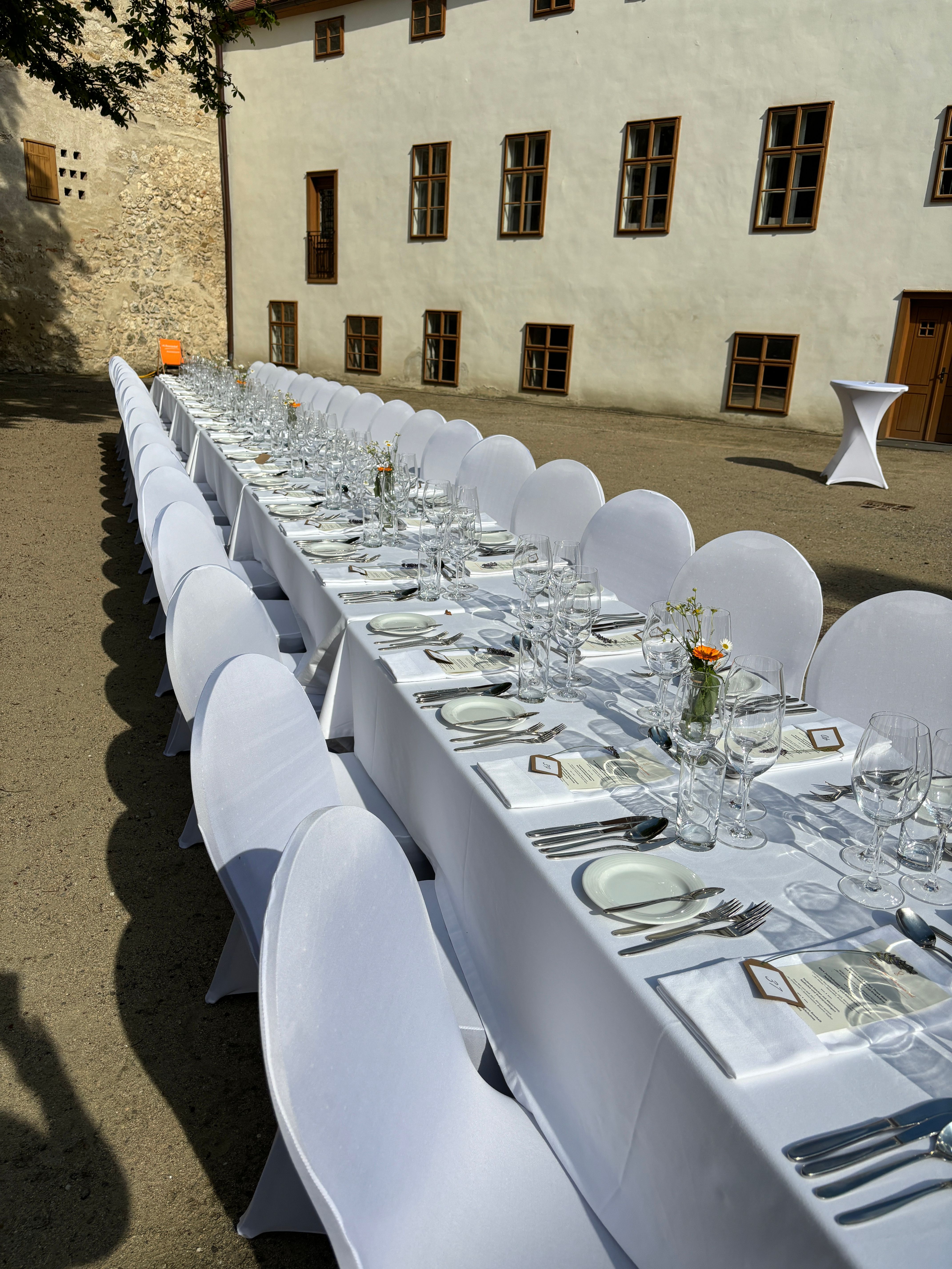 Lange, festlich gedeckte Tafel im Freien vor einem historischen Gebäude.