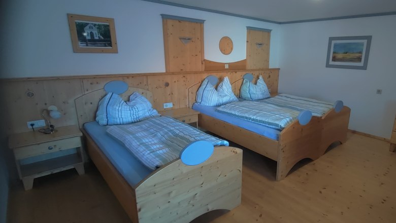 Gemütliches Schlafzimmer mit zwei Einzelbetten aus Holz, Nachttisch und Kommode.