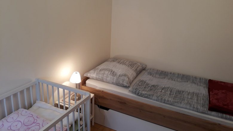Einzelzimmer mit Einzelbett, Kinderbett und Nachttischlampe.