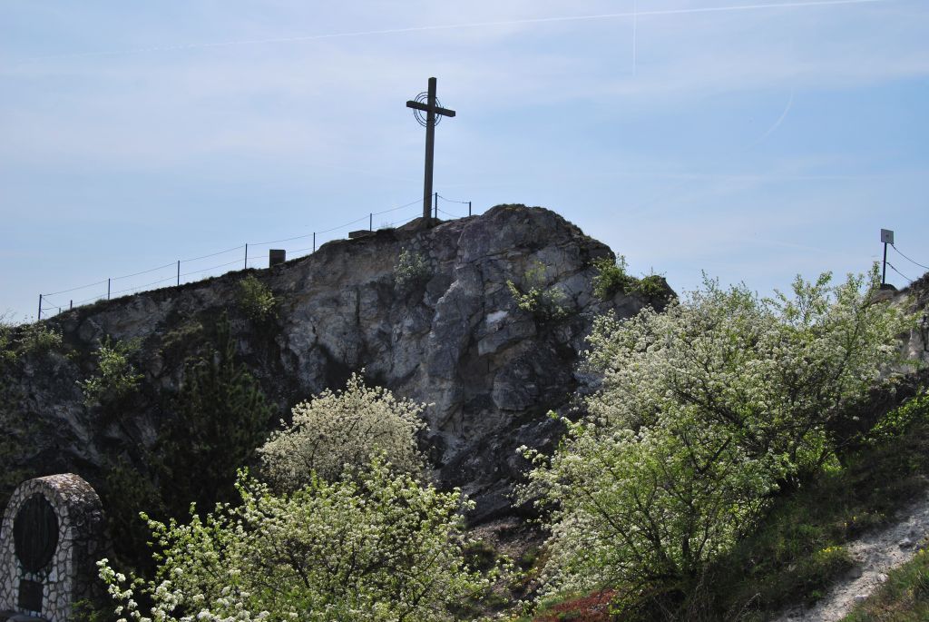 Na kopci stojí kříž a v popředí jsou rozkvetlé stromy.