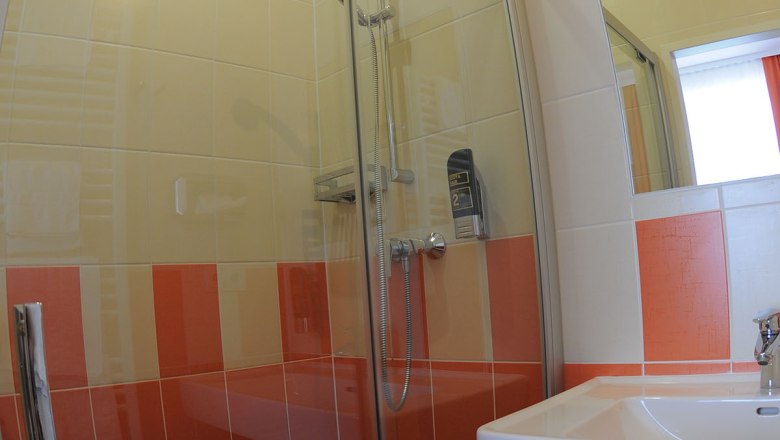 Badezimmer mit Dusche, Waschbecken und orange-wei&szlig;en Fliesen.