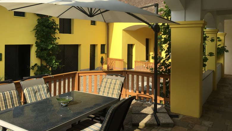 Terrace with table, chairs and parasol in front of yellow building.