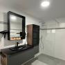 Modern bathroom with black washbasin, mirror, rain shower and gray tiles.