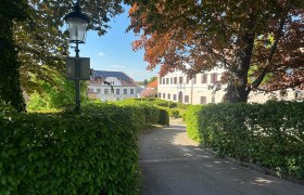 Ansicht eines Schlosses in Großrußbach, umgeben von Bäumen und Hecken, mit einer Laterne im Vordergrund.
