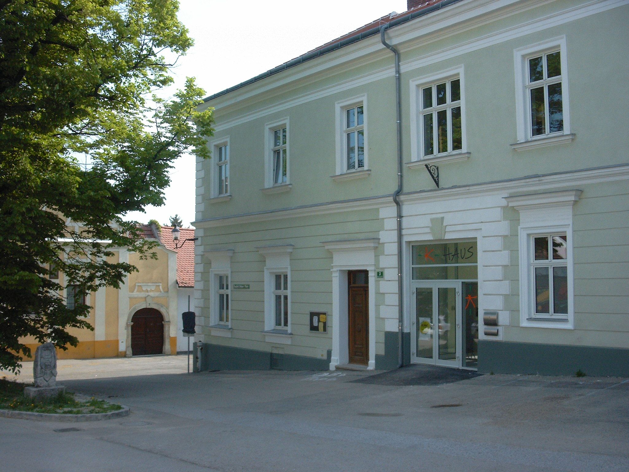 Dvojpodlažná, svetlozelená budova s nápisom "dom" nad dverami.