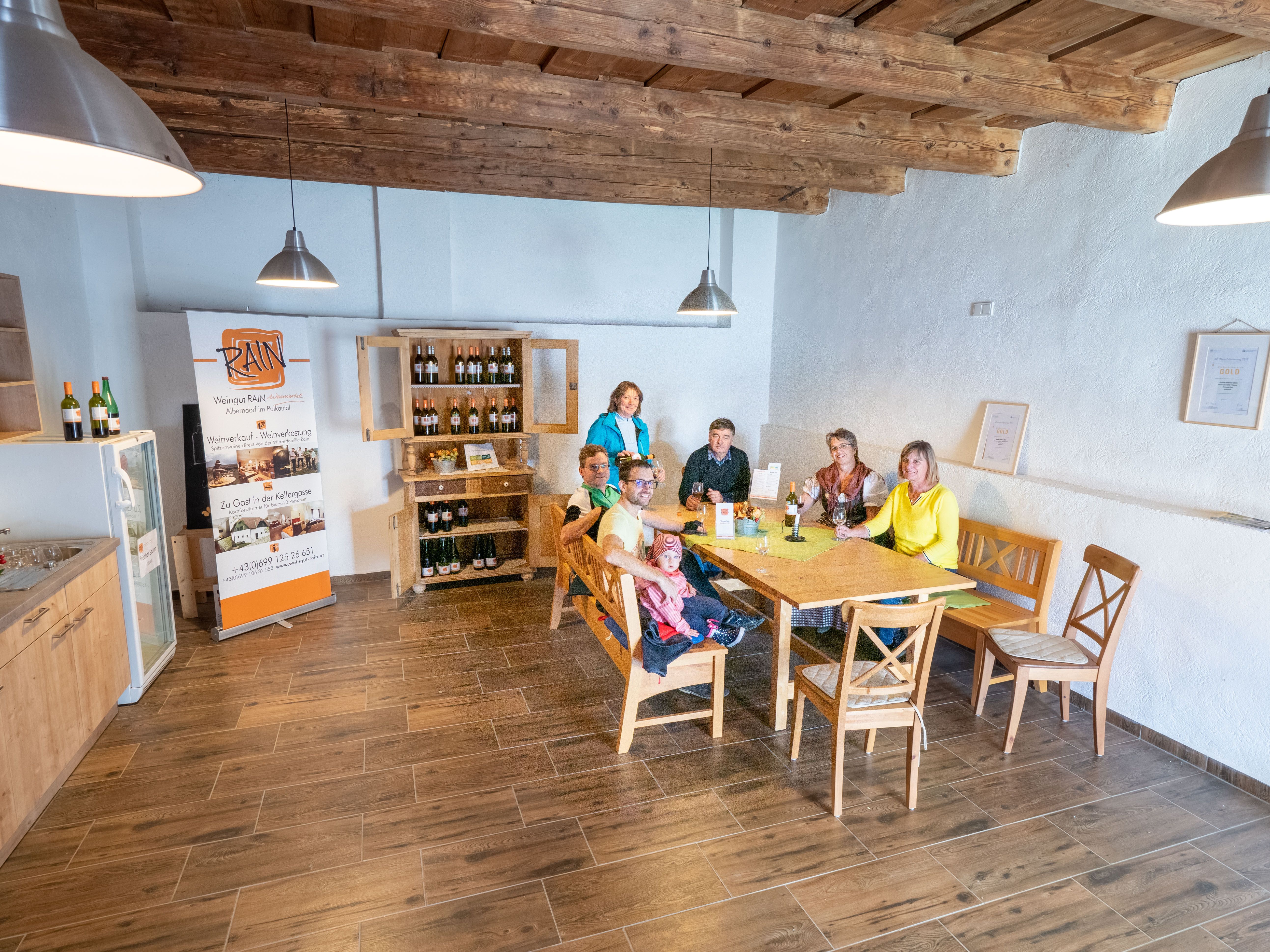 Eine Gruppe von Menschen sitzt an einem Tisch in einem gemütlichen Raum mit Holzboden und -decke.