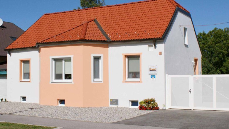 Ein kleines, einstöckiges Haus mit orangefarbenem Dach und weißer Fassade unter blauem Himmel.