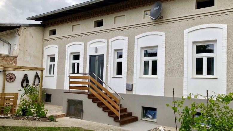 Ein renoviertes Haus mit weißen Fenstern und einer Holztreppe, umgeben von einem kleinen Garten mit Pflanzen.